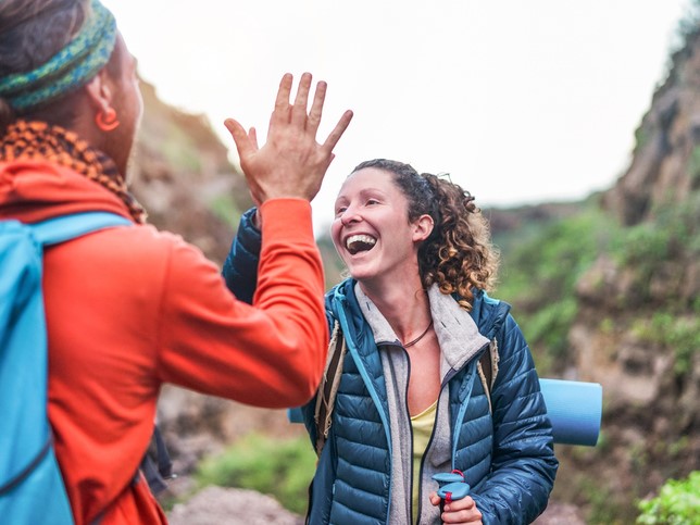 To kvinner er på tur i fjellet. De smiler og gir hverandre en hi-five.