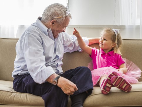 En bestefar leker med barnebarnet sitt. De har begge prinsessekroner på hodet. Barnebarnet har også rosa tyllskjørt.