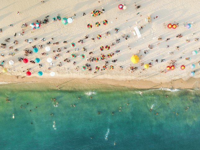 Flyfoto av en overfylt strand, parasoller og mennesker på sanden.